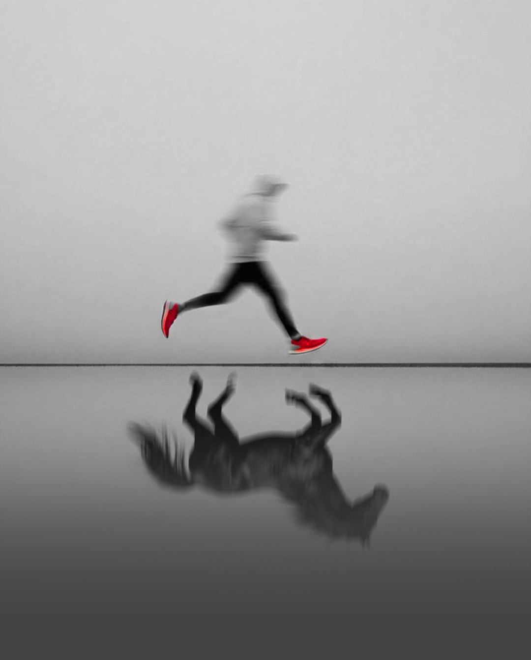 A blurred runner in red shoes mid-stride above a still, misty horizon, with a dark horse-like reflection in the water below