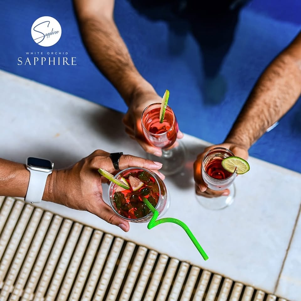 Hands holding cocktails over a table at White Orchid Sapphire